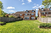 Room: Garden Back | A well-maintained outdoor yard featuring a house, tree, and landscaped grass area under a cloudy sky.