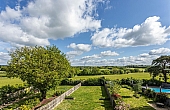 Room: Garden Back | This photo shows an outdoor garden area with lush grass, trees, and a clear sky.