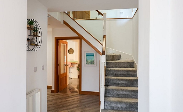 Room: Ground Floor Hall | An indoor staircase with a wooden handrail and balusters, featuring detailed molding and a clean, well-maintained floor. | Accessibility: Photograph showing an indoor staircase with a polished wooden handrail and matching balusters, detailed molding along the wall, and a clean, light-colored tiled floor illuminated by natural light.