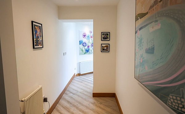 Room: Ground Floor Hallway | An indoor room featuring stairs, a picture frame with art on the wall, and a polished floor. | Accessibility: Photograph showing an indoor room with a staircase, a wall-mounted picture frame containing artwork, and a polished wooden floor illuminated by natural light.