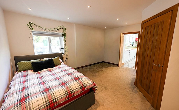 Room: bedroom | A well-presented bedroom featuring a bed with linens, pillows, and a bed frame on a clean floor. | Accessibility: Photograph showing a bedroom with a bed positioned against a wall, covered with white linens and pillows, a wooden bed frame, a clean floor, and soft lighting illuminating the room's neutral color scheme.