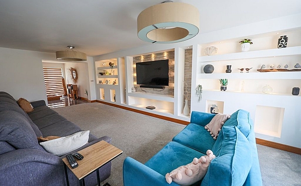 Room: Living Area | A well-maintained living room featuring a sofa bed, loveseat, coffee table, television, and decorative pillows. | Accessibility: Photograph showing a living room with a neutral-colored sofa bed and loveseat, a wooden coffee table, a television on the wall, decorative pillows on the seating, and soft, ambient lighting illuminating the space.