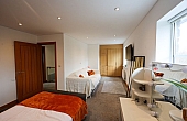 Room: bedroom | A well-maintained bedroom featuring a bed with linens and a bed frame. | Accessibility: Photograph showing a bedroom with a wooden bed frame, topped with white linens and a neatly made bed, illuminated by natural light from a window, with light-colored walls and a simple interior design.