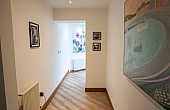 Room: Ground Floor Hallway | An indoor room featuring stairs, a picture frame with art on the wall, and a polished floor. | Accessibility: Photograph showing an indoor room with a staircase, a wall-mounted picture frame containing artwork, and a polished wooden floor illuminated by natural light.