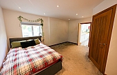 Room: bedroom | A well-presented bedroom featuring a bed with linens, pillows, and a bed frame on a clean floor. | Accessibility: Photograph showing a bedroom with a bed positioned against a wall, covered with white linens and pillows, a wooden bed frame, a clean floor, and soft lighting illuminating the room's neutral color scheme.