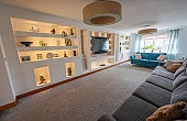 Room: Living Area | A cozy indoor room featuring a sofa bed, a loveseat, pillows, shelving, and a clean floor and ceiling. | Accessibility: Photograph showing a cozy indoor room with a light-colored sofa bed and matching loveseat, adorned with pillows, against a wall with shelving, illuminated by soft, natural lighting, with a clean, smooth floor and ceiling.