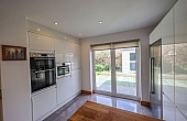 Room: kitchen | A well-maintained kitchen featuring laminate flooring, cabinetry, a countertop, a window, and a kitchen appliance. | Accessibility: Photograph showing a well-maintained kitchen with light-colored laminate flooring, white cabinetry with silver handles, a beige countertop, a window allowing natural light, and a stainless steel kitchen appliance.