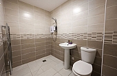 Room: Bathroom | A clean, white bathroom featuring a toilet, sink, and tiled floor. | Accessibility: Photograph showing a bright, white bathroom with a tiled floor, a white ceramic toilet and sink, and ample natural or artificial lighting illuminating the clean, smooth surfaces and neutral color scheme.
