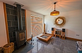 Room: Living Area | A well-maintained indoor den featuring hardwood flooring, cabinetry, a coffee table, and a ceiling fan. | Accessibility: Photograph showing a well-maintained indoor den with light-colored hardwood flooring, built-in cabinetry along the wall, a wooden coffee table, and a ceiling fan with a light fixture, illuminated by natural and artificial lighting.